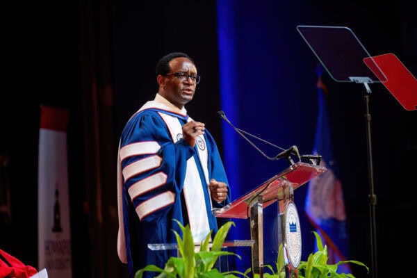 Ben Vinson III speaks from a lectern, wearing blue and white academic regalia.
